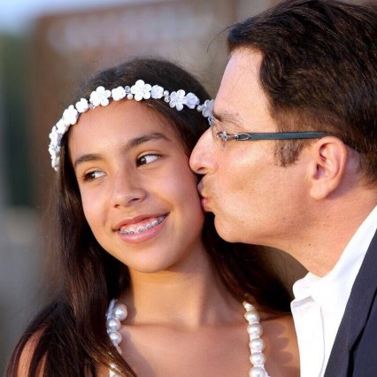 Dad kisses preteen daughter on the cheek, both dressed up for a special occasion.