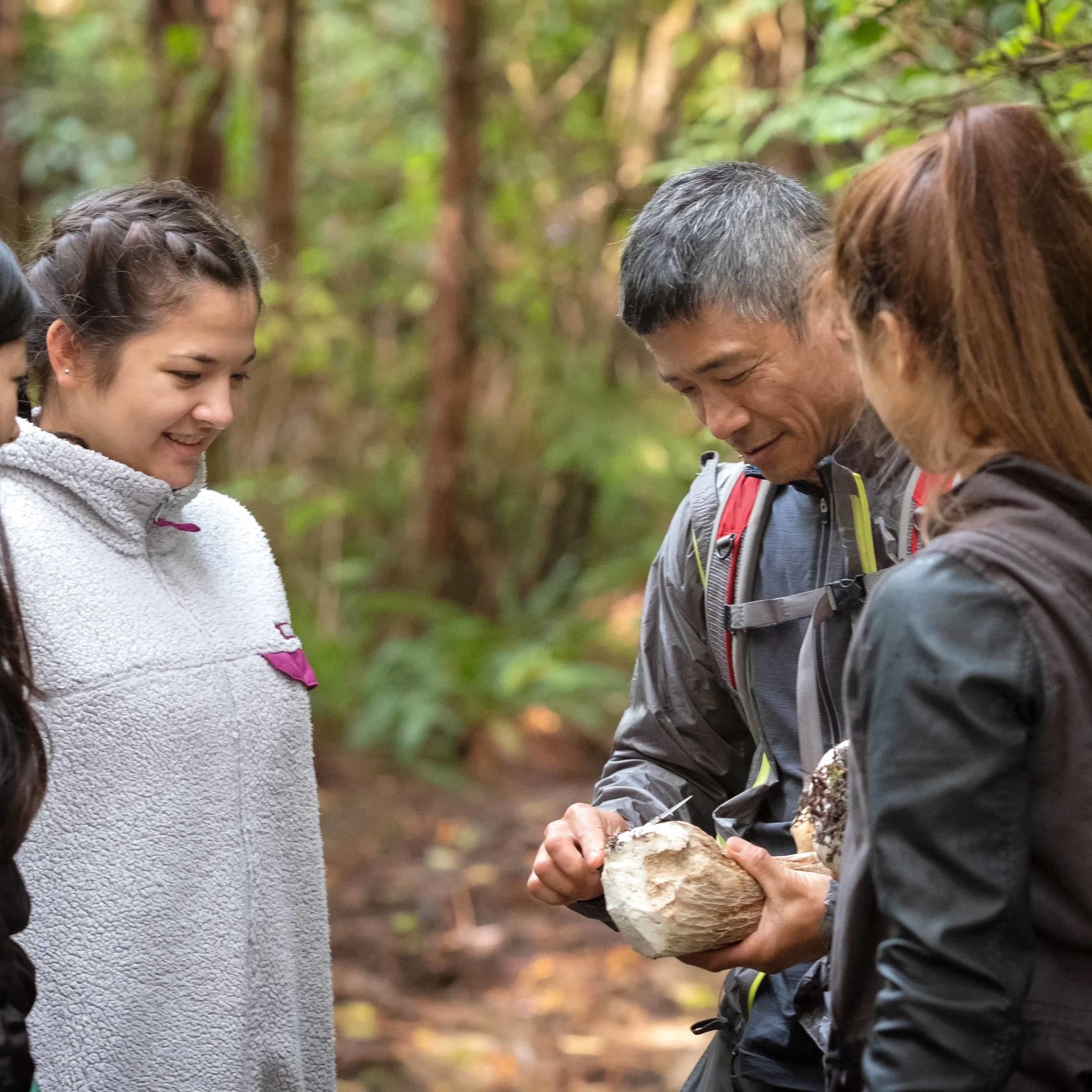 Group of teens with a mentor stop on a hike to whittle a piece of wood.