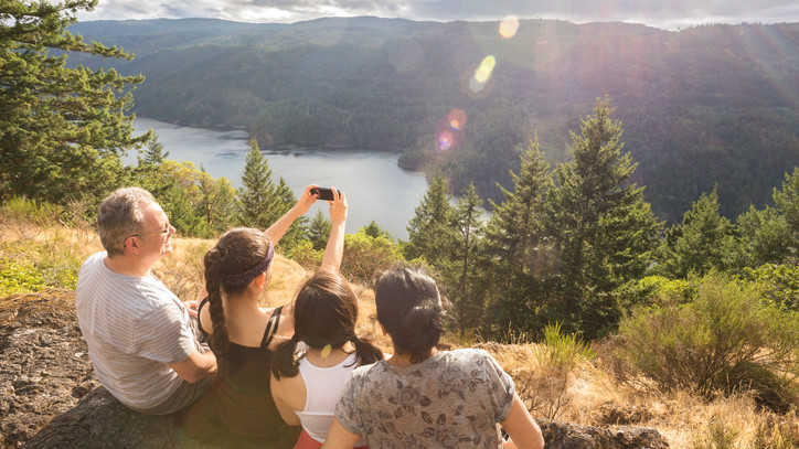 A teenage girl taking selfie photo of her family after hiking to top of mountain.