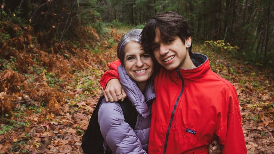 Mom and teenage son share a hug in a fall forest setting.