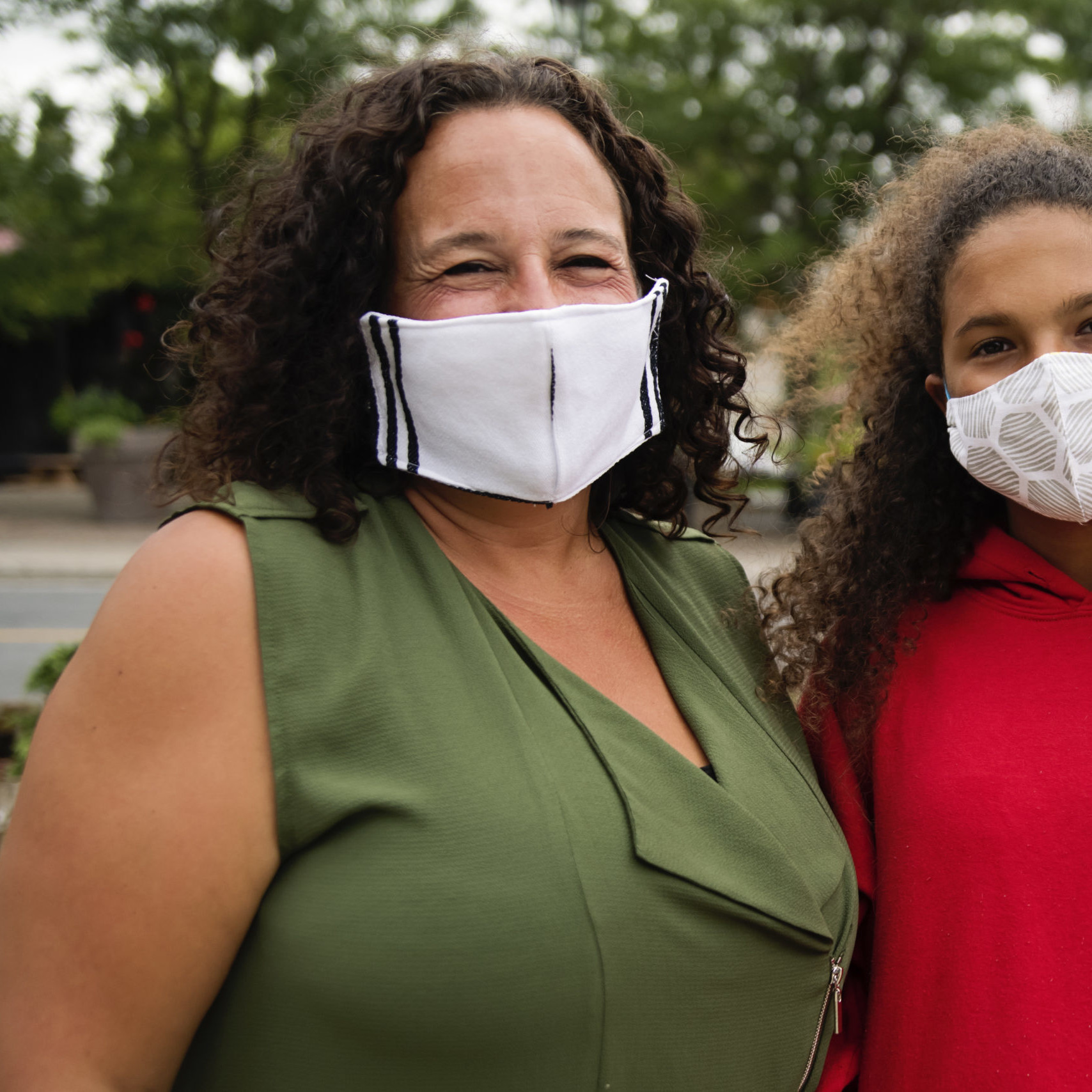 Mature mother and teenage mixed-race daughter wearing protective face mask before entering a store in small city street. Both have very curly brown hair. Horizontal waist up outdoors shot with copy space.