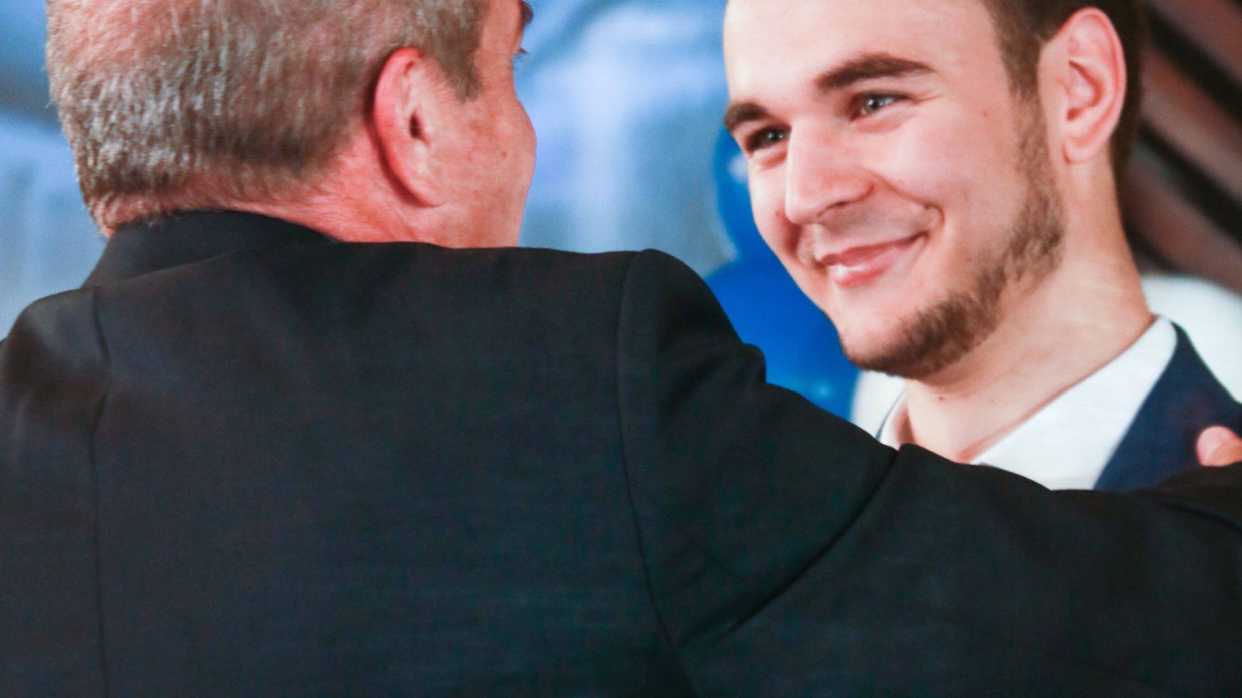 Mentor places hand on the shoulder of a smiling young man. Affirmations are being exchanged.