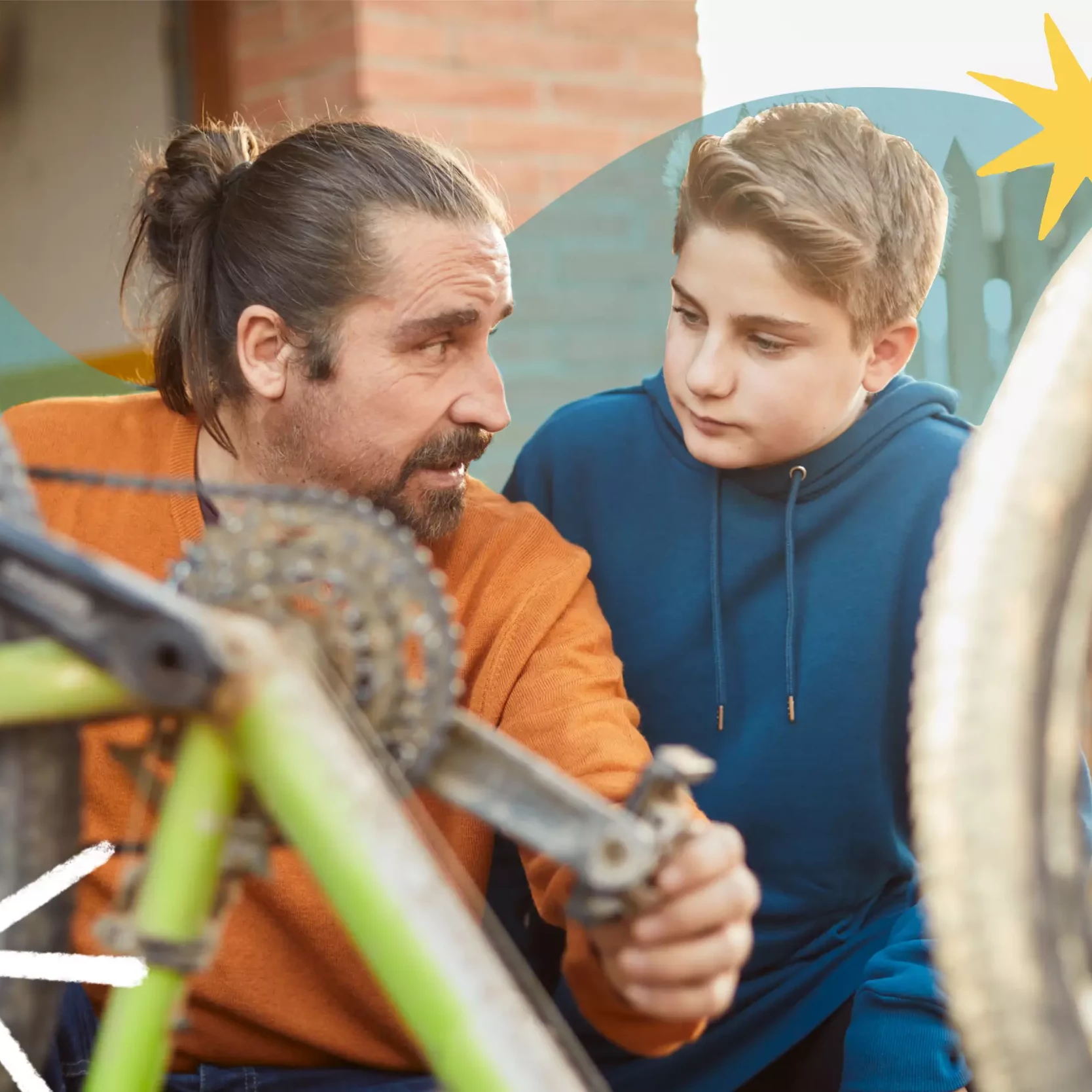 Dad looks toward his son as he teaches him how to fix a bike