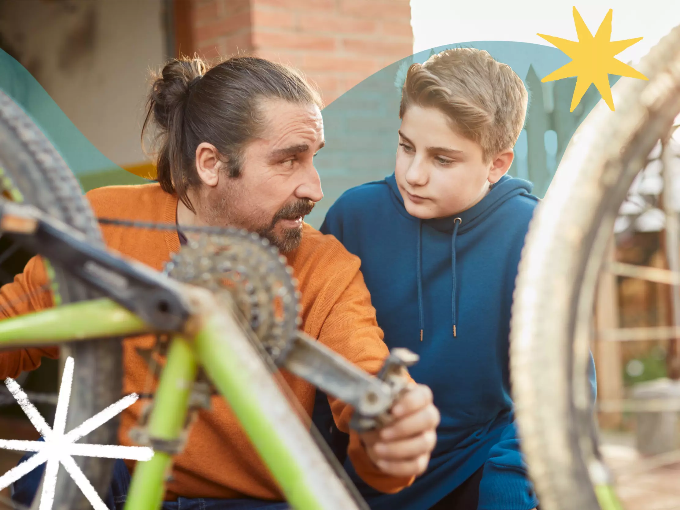 Dad looks toward his son as he teaches him how to fix a bike
